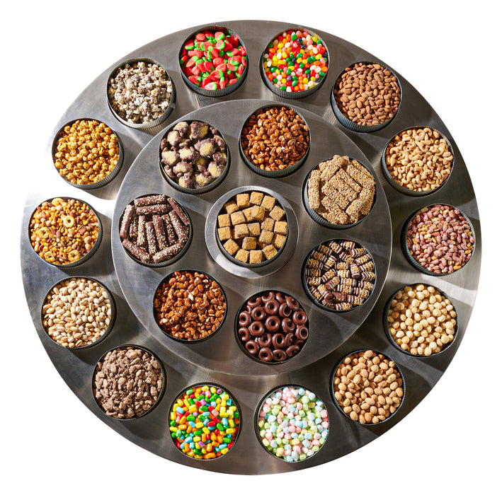 A top-down view of The Nuttery’s round table showcasing a variety of colorful candies, chocolates, and nuts in metal tins, elegantly organized for a festive presentation