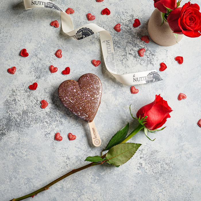 A glittery heart-shaped chocolate pop, perfect for Valentine’s Day. Surrounded by romantic red roses and heart decorations, this sweet treat makes a heartfelt gift.