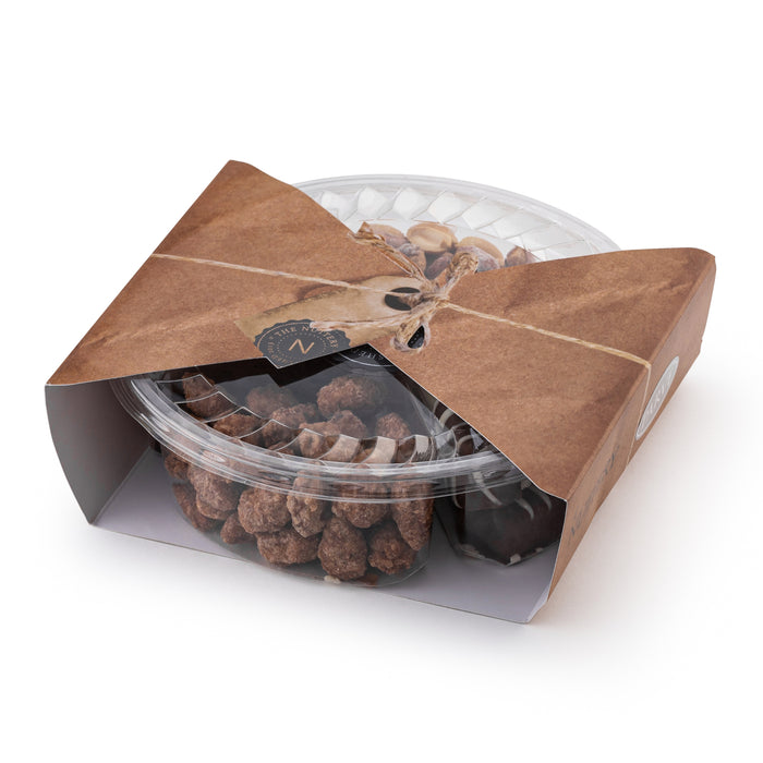 The Nuttery NY chocolate and nut gift tray, elegantly packaged in a clear plastic container with rustic kraft paper wrapping and twine, featuring an assortment of gourmet chocolates and roasted nuts