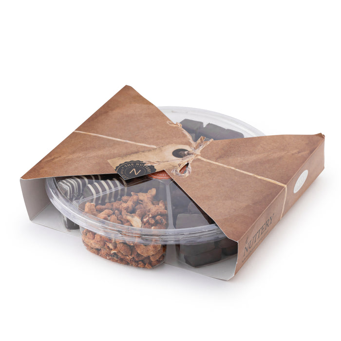 The Nuttery NY chocolate and nut gift tray, elegantly packaged in a clear plastic container with rustic kraft paper wrapping and twine, featuring an assortment of gourmet chocolates and roasted nuts.